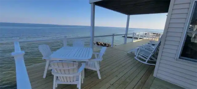 Photo of wooden deck along water with outdoor furniture.