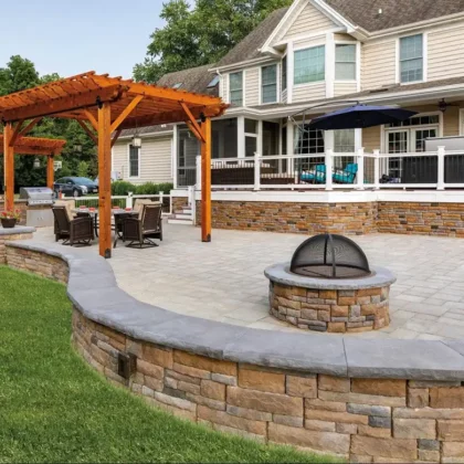 Photo of covered deck/porch with paver patio, fire pit, outdoor kitchen, and wooden pergolas.
