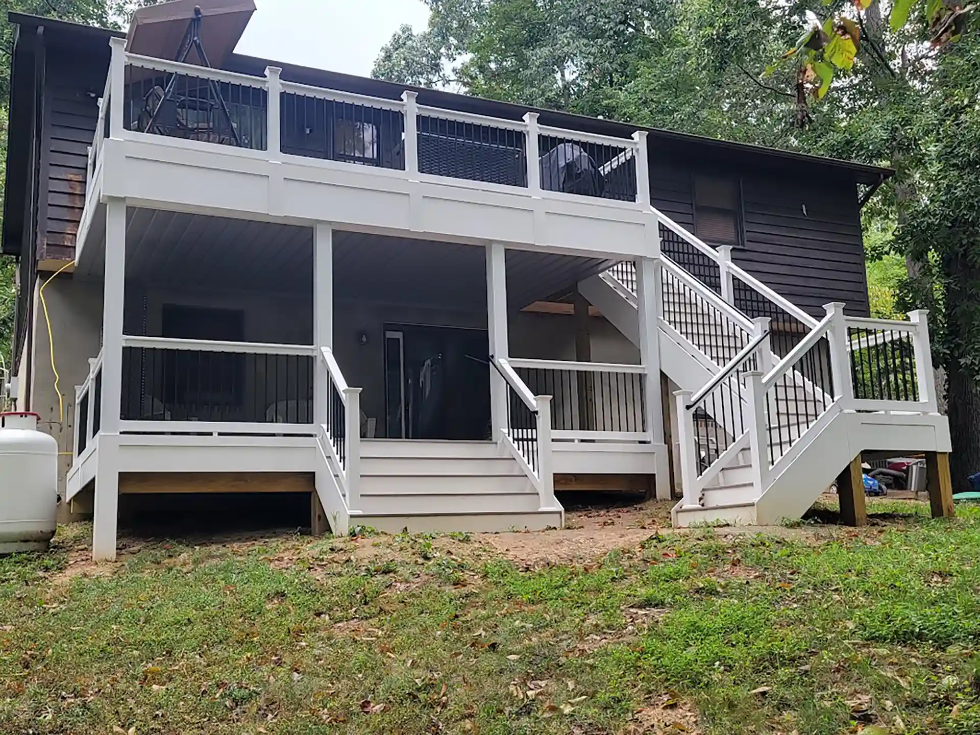 Two-story white deck with black baluster railings, an underdeck ceiling system, and dual staircases attached to a dark brown house.
