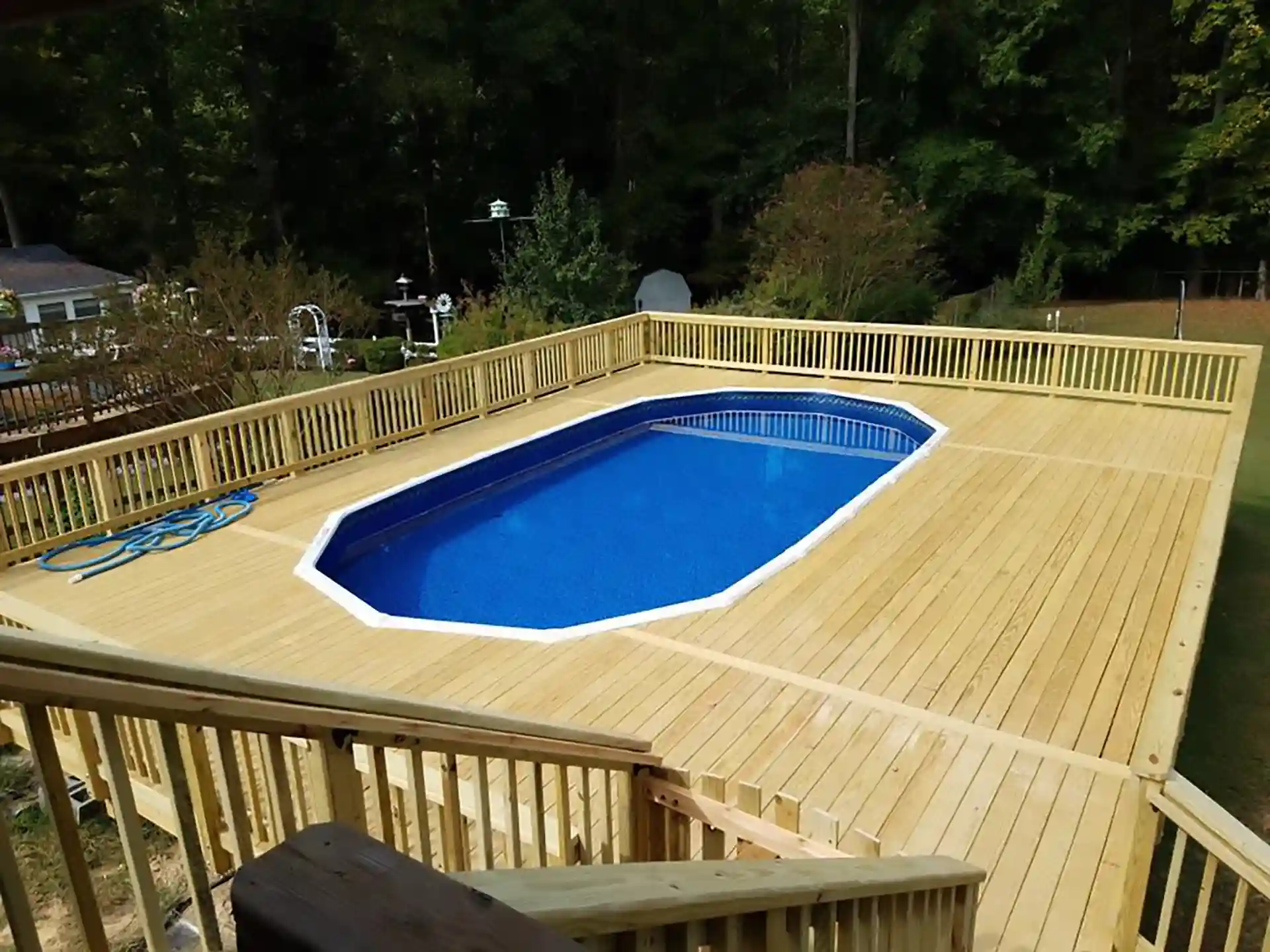 Wooden deck surrounding an above-ground pool with railing and stairs leading down.
