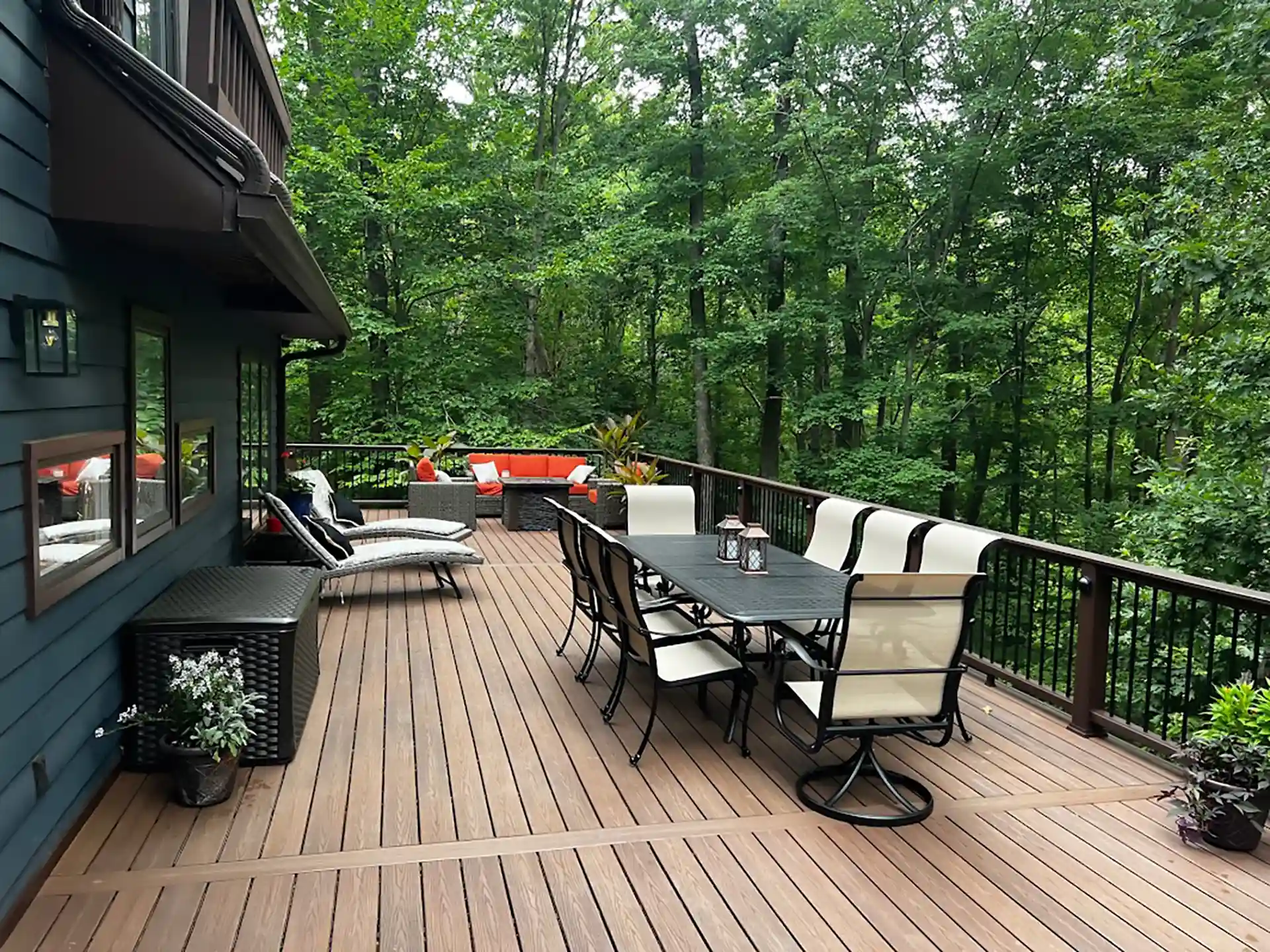 Spacious composite deck with outdoor dining and lounge seating, surrounded by a wooded landscape.
