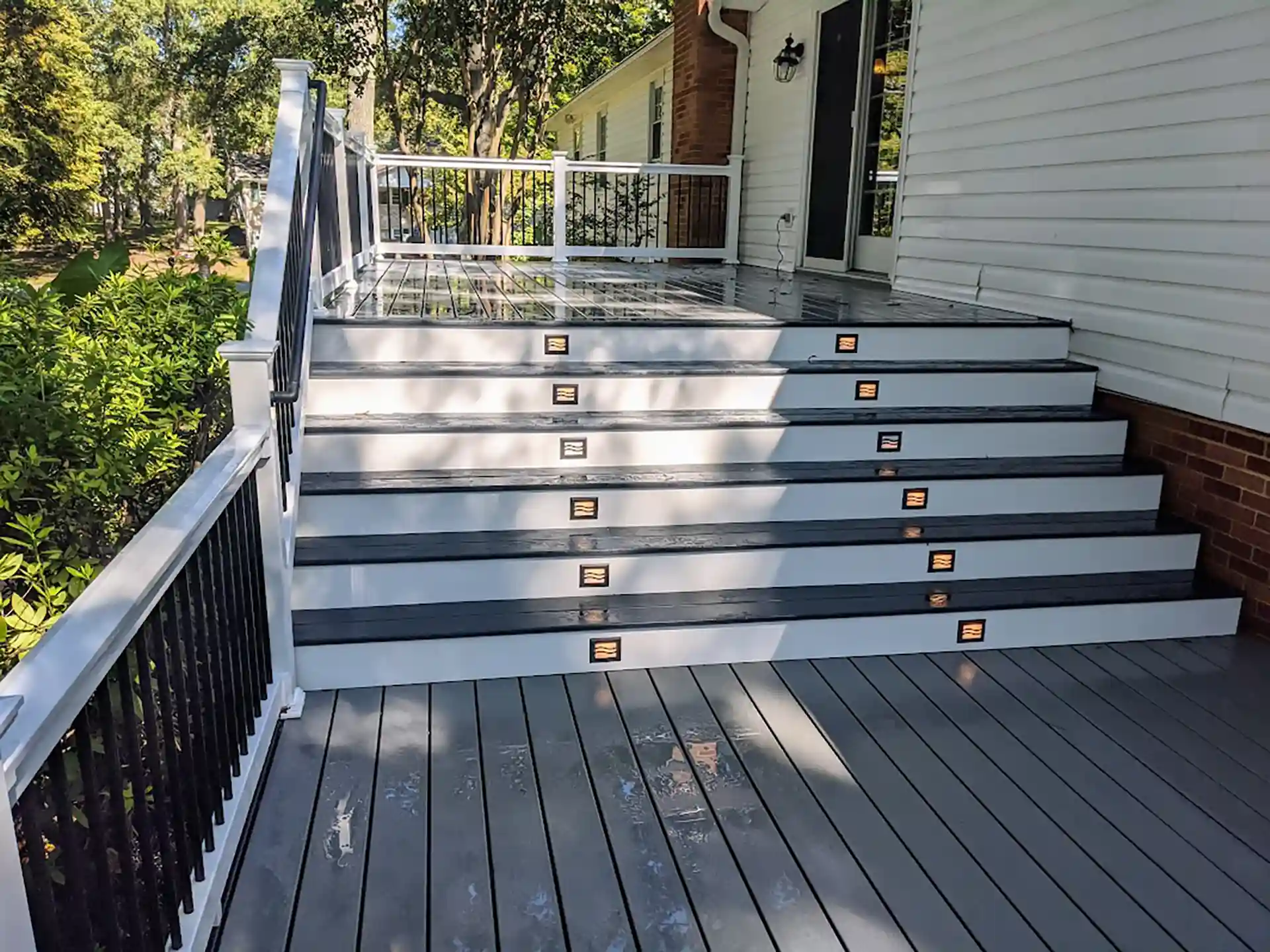 Gray composite deck with wide illuminated staircase, white and black railing, and a modern design.
