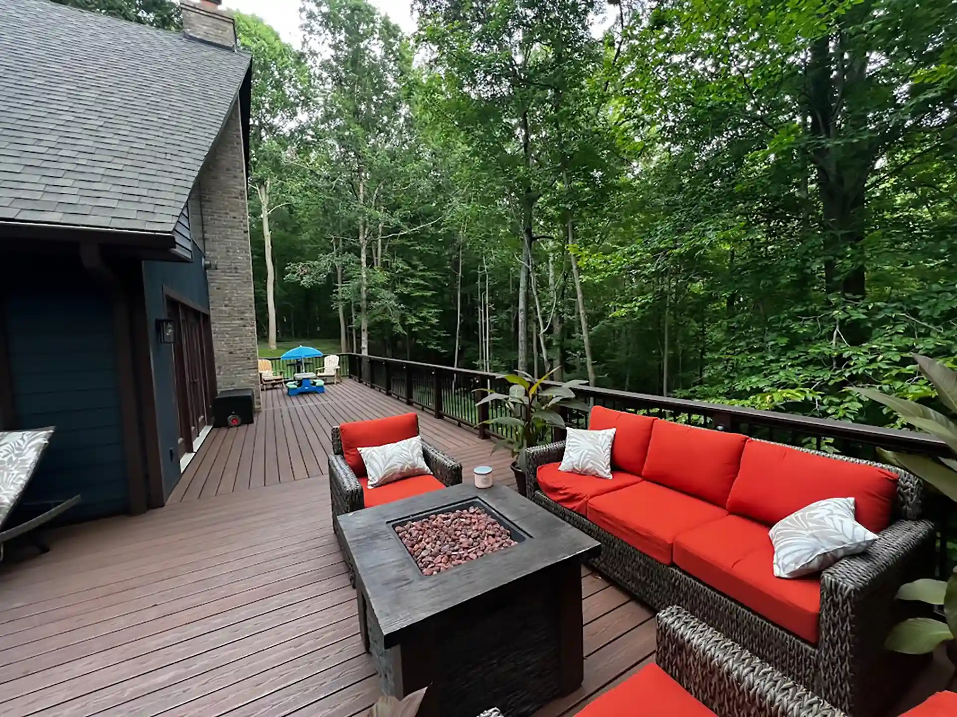Deck with red cushions and a fire table, surrounded by trees and lush greenery
