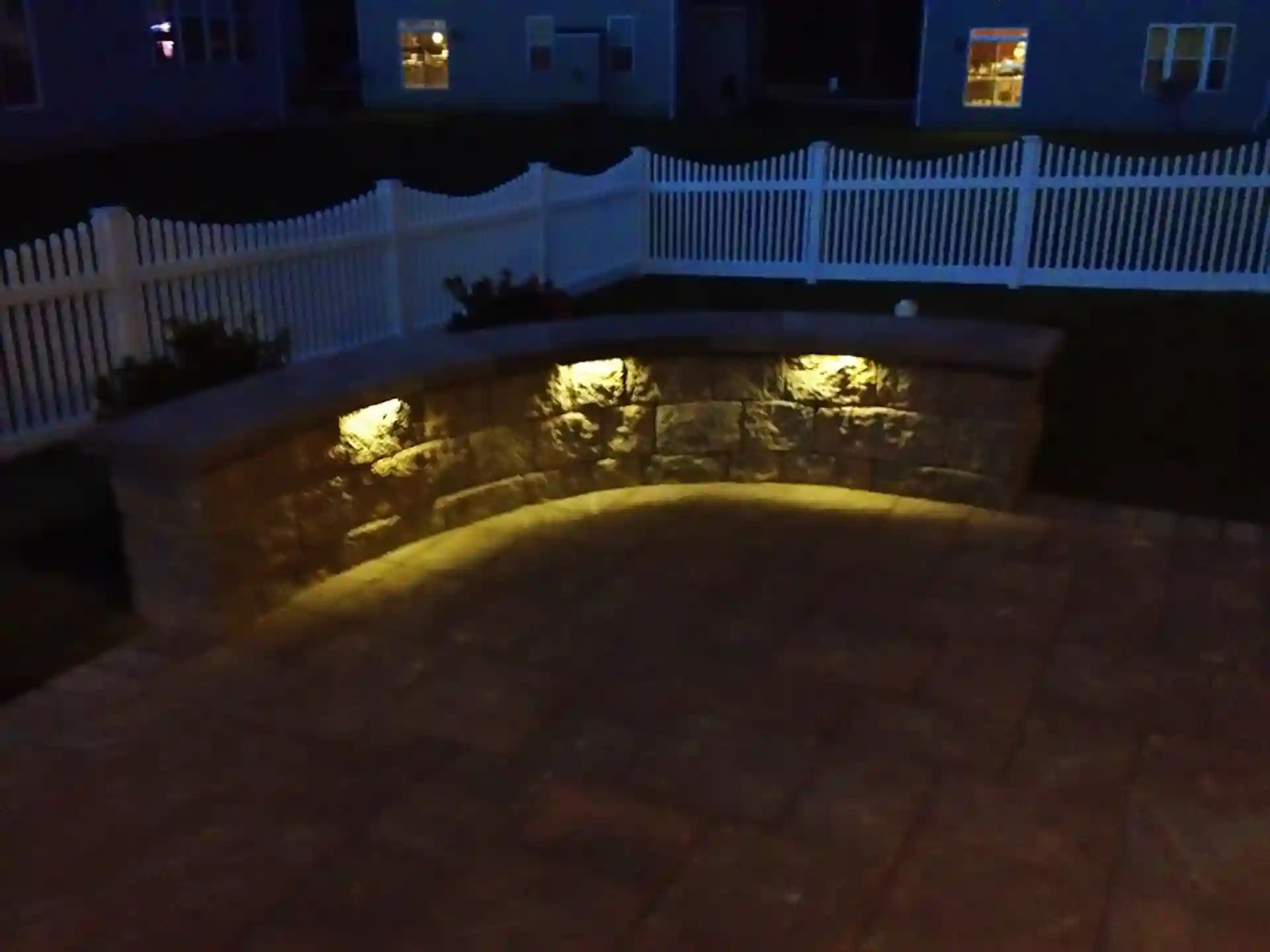 Stone seating wall with built-in lighting, set against a white fence in the evening.