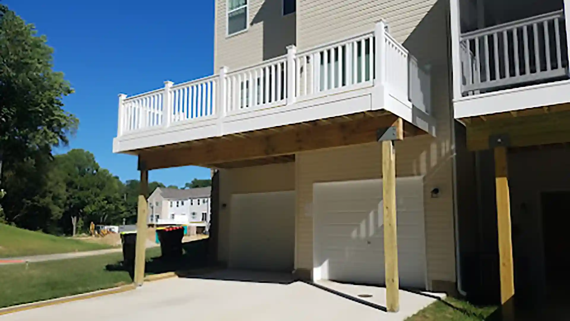 Raised deck with white railings, supported by wooden posts beneath a multi-story home