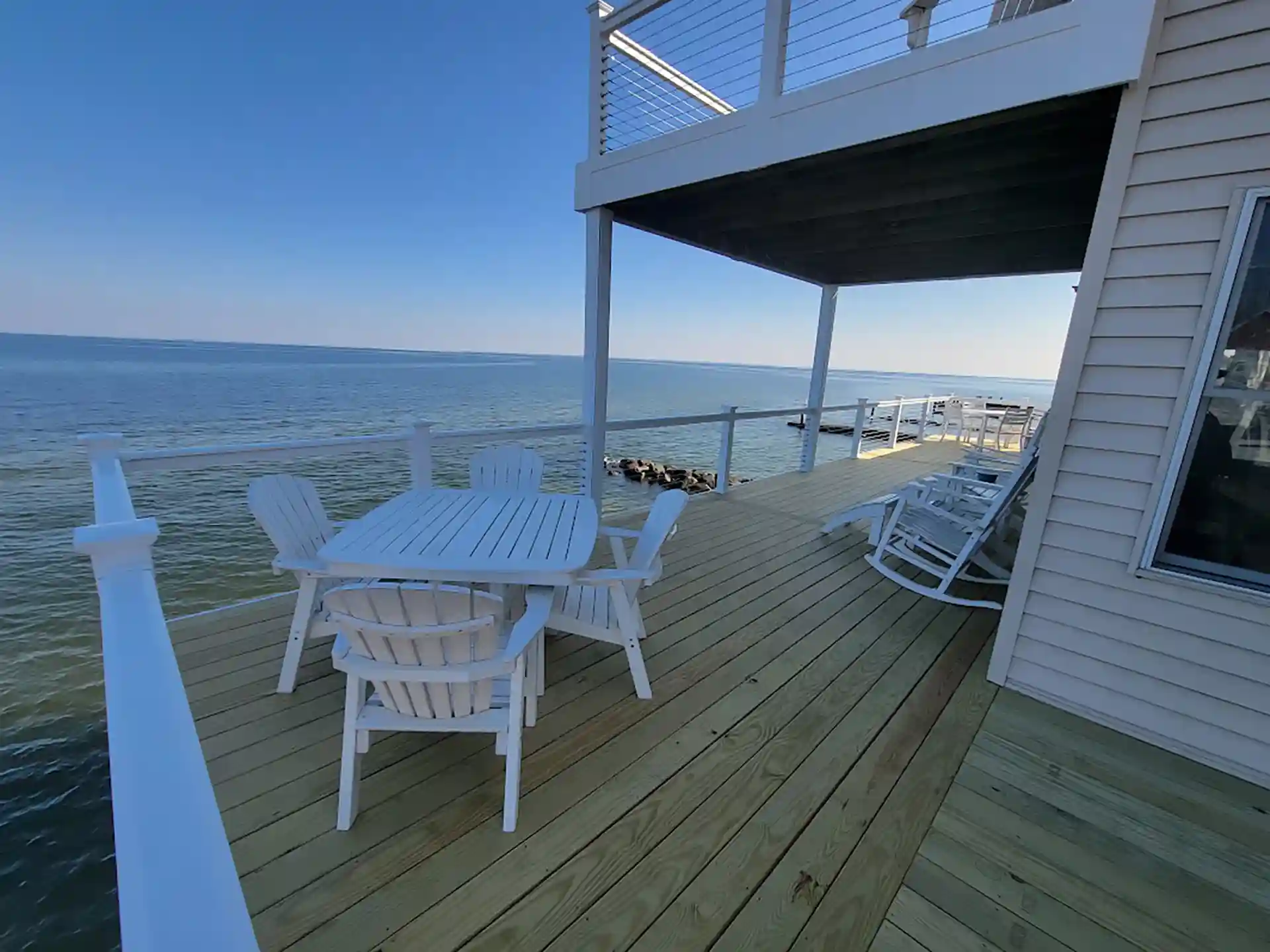 Seaside deck with white furniture, overlooking the water and supporting a second-story structure.