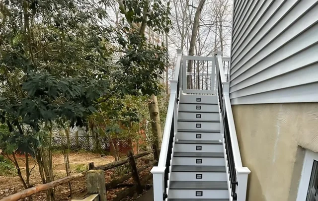 Modern white deck stairs with gray treads and built-in lighting, leading up to a house.