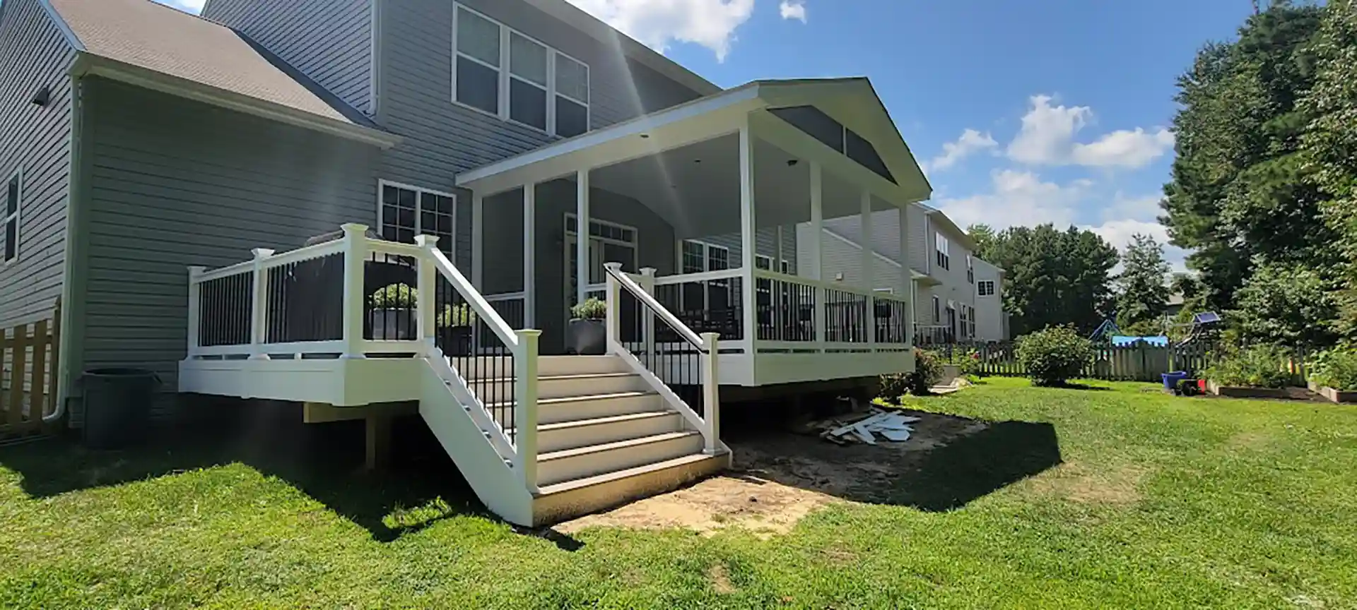 Covered back porch with white railings, black balusters, wide stairs, and a gable roof attached to a two-story house. 