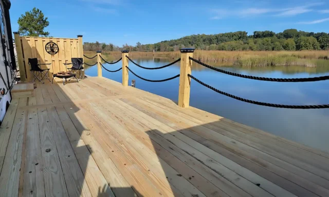 A wooden deck with rope railings and chairs, overlooking a body of water.